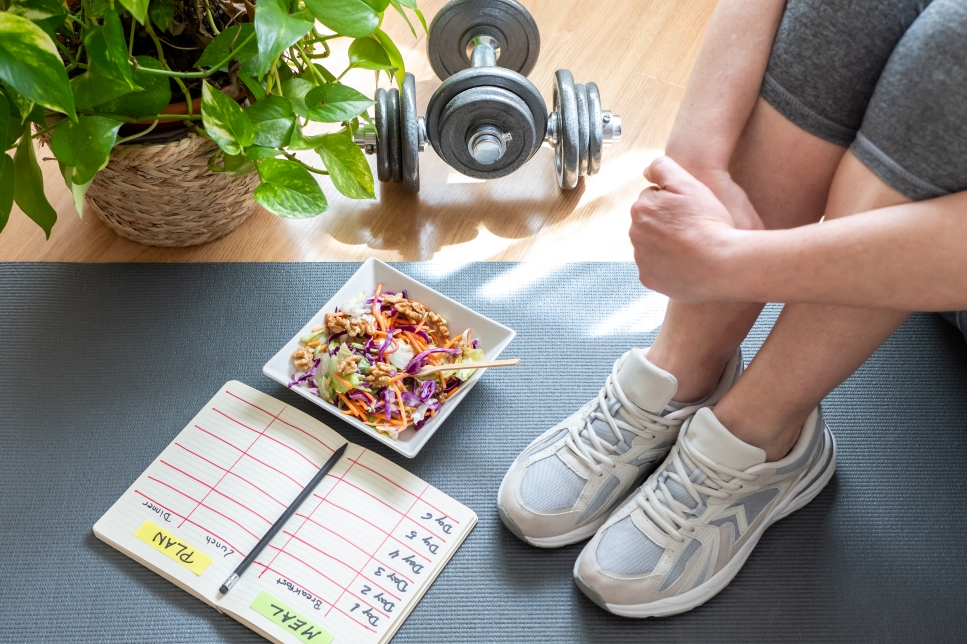 woman sitting on yoga mat with salad and meal plan notebook
